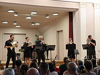 Fünf Musiker einer Bläsergruppe spielen stehend auf der Bühne im Musikschulkonzert.