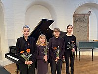 Gruppenfoto mit vier Musikschülerinnen, die in Konzertkleidung mit einer Blume in der Hand vor einem Flügel stehen.