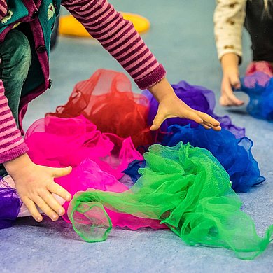 Kinderhände wühlen in einem Haufen bunter Tücher