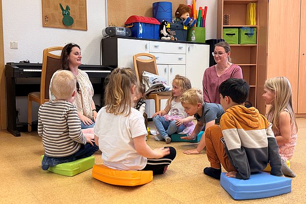 Kinder sitzen im Kreis am Boden und singen