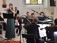 Eine junge Blockflötistin im grünen Kleid musiziert mit der Kammerphilharmonie.