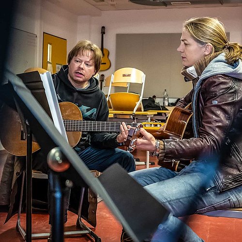 Erwachsene Gitarrenschülerin und Gitarrenlehrer spielen gemeinsam in einem Musikraum