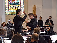 Dirigent und jugendlicher Trompeter in der Bildmitte umgeben von Profis der Kammerphilharmonie.