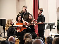Fünf Mädchen und Jungen musizieren gemeinsam auf einer einzigen Gitarre.